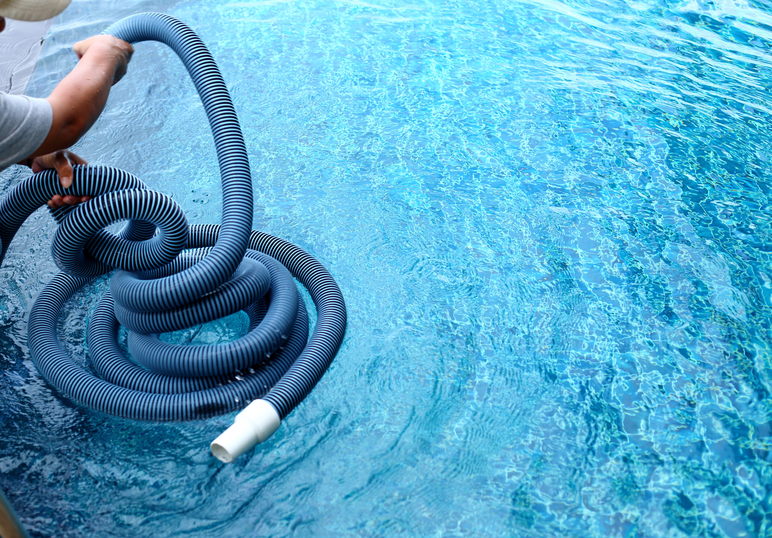 Woman Worker clean private swimming pool with vacuum blue tube cleaner every week in Summer